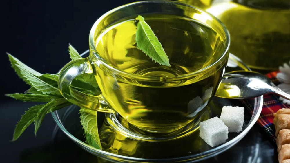یک فنجان شیشه ای و نعلبکی چای سبز همراه با قند