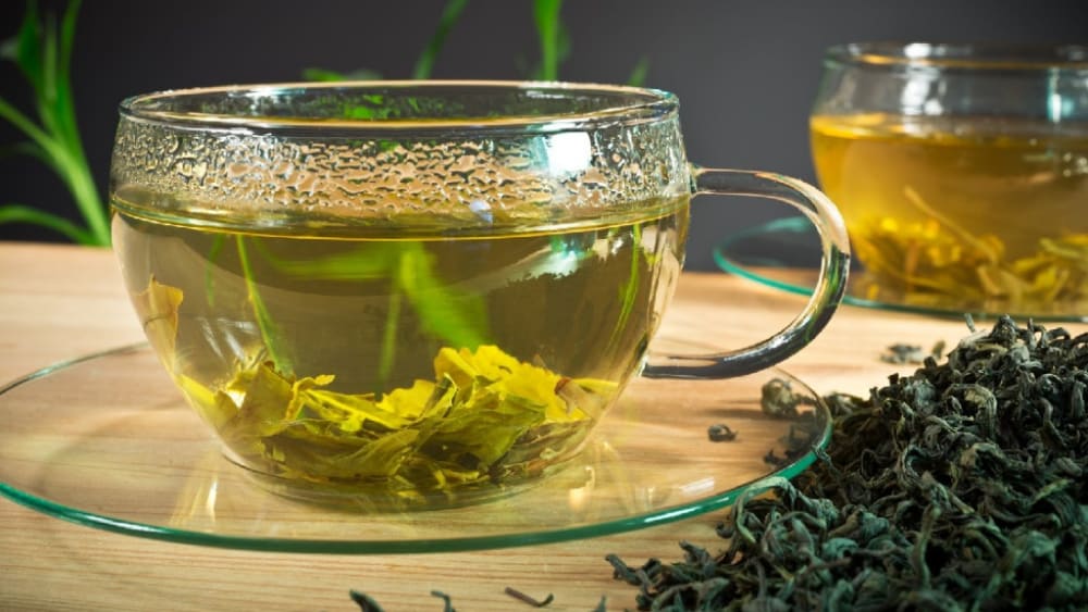 یک فنجان چای سبز همراه با مقداری چای سبز خشک‌ روی میز