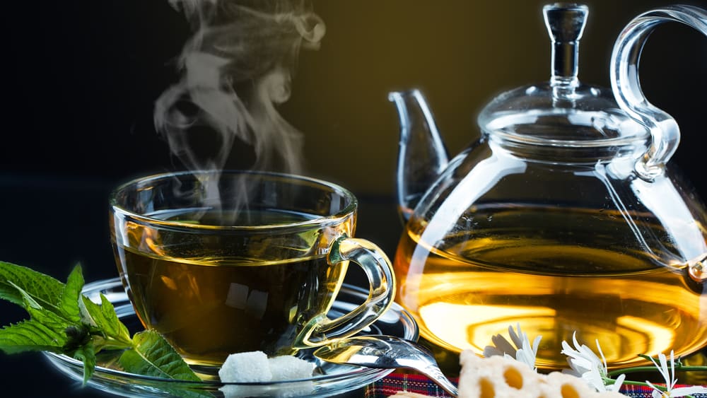 فنجان و قوری شیشه ای حاوی چای سبز داغ که از آن بخار می آید؛ مرتبط با مقایسه چای سبز و قهوه