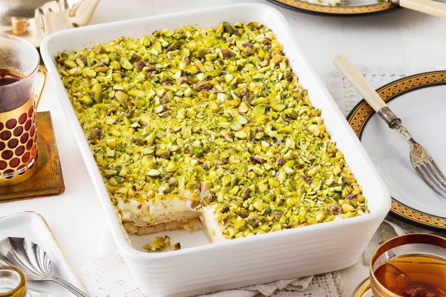 عکس از نمای بالا از دسر عیش السریا، شیرینی عربی تزئین شده با پسته خرد شده در ظرف سفید.