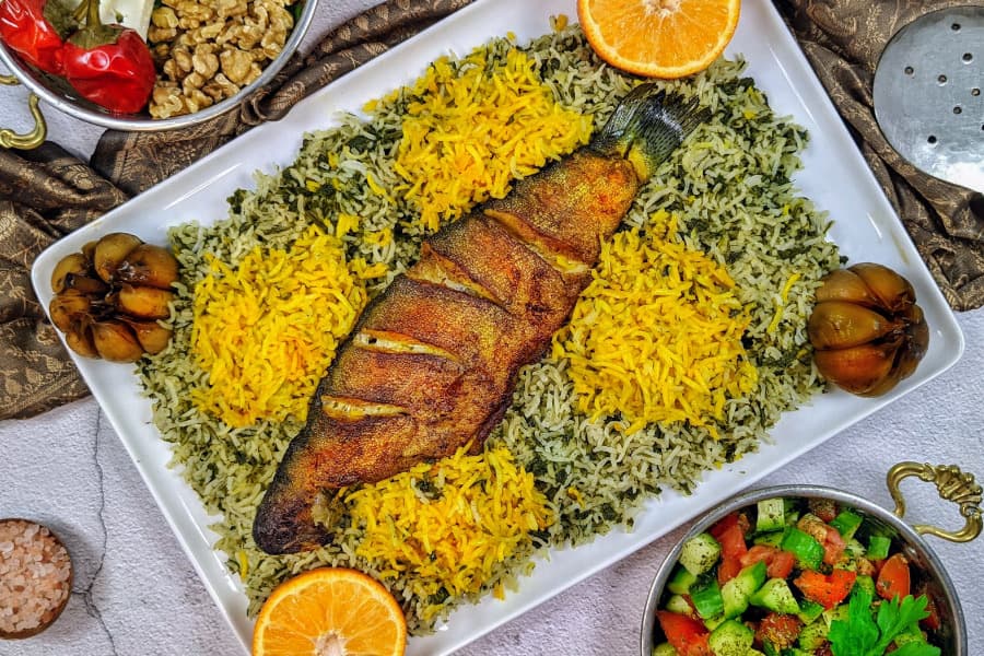 یه دیس سبزی پلو با ماهی سرخ شده، با برنج زعفرونی، سیرترشی و پرتقال، کنار سالاد شیرازی، یه غذای خوشمزه که شب عید تو شهرای مختلف ایران درست میشه