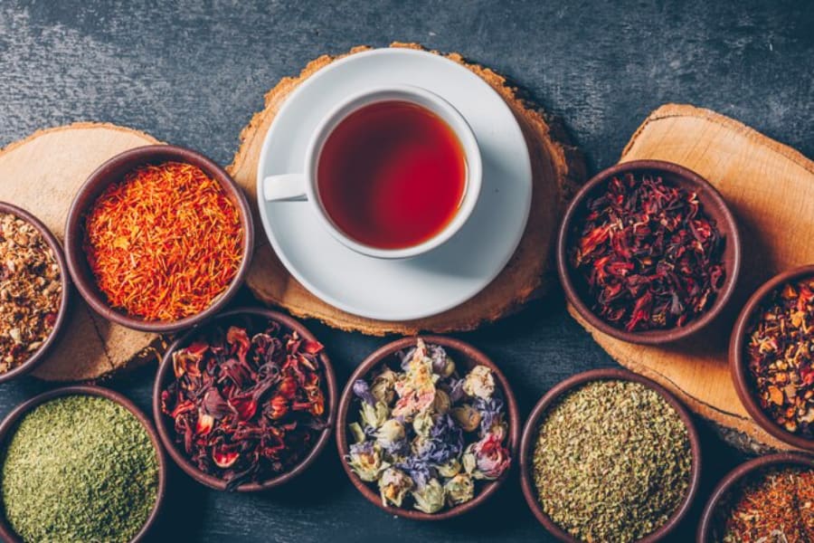 یک‌ فنجان چای خوش رنگ همراه با ظرف های کوچکی حاوی گل های خشک شده و پودر گیاهان خشک