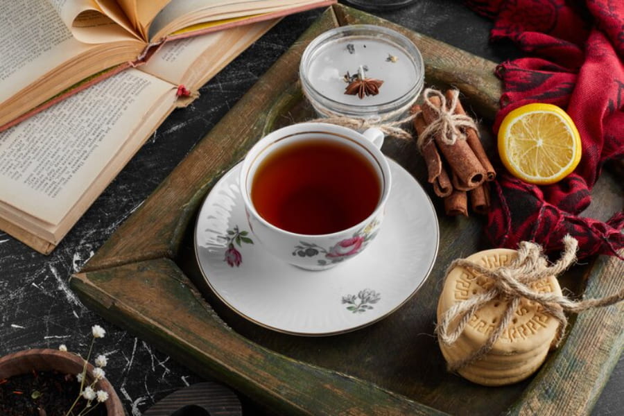 یک فنجان چای با چوب دارچین و بیسکویت داخل سینی چوبی