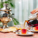 زنی در حال ریختن چای از قوری داخل استکان کمر باریک