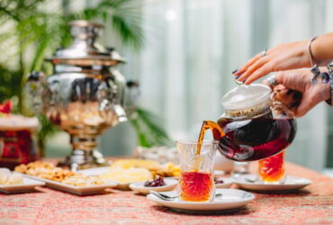 زنی در حال ریختن چای از قوری داخل استکان کمر باریک