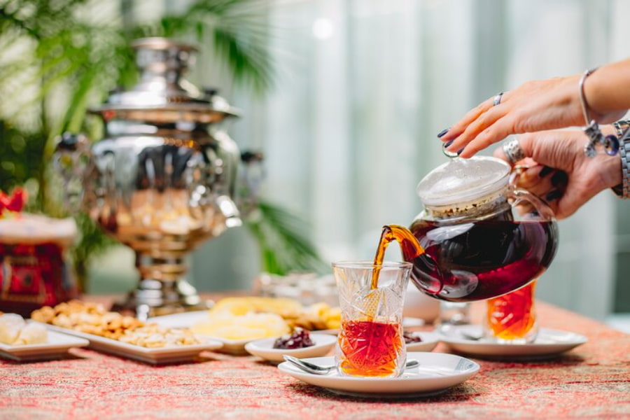 زنی در حال ریختن چای از قوری داخل استکان کمر باریک